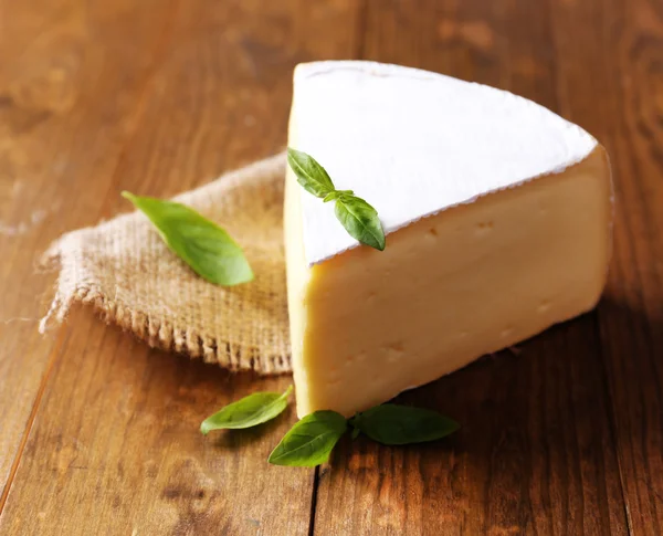 Tasty Camembert cheese with basil, on wooden table — Stock Photo, Image