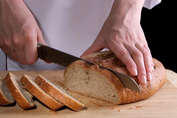 Cutting bread on wooden board on dark background — Stock Photo, Image