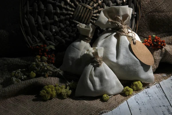 Sachet textile avec fleurs séchées, herbes et baies sur table en bois, sur fond de sac — Photo