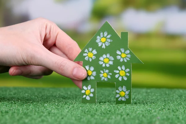 Pequena casa de papel na mão na grama verde no fundo brilhante — Fotografia de Stock
