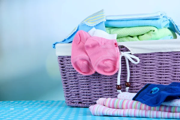 Pilha de roupas de bebê na cesta, na mesa no fundo de cor — Fotografia de Stock