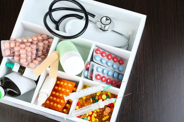 Pastillas médicas, estetoscopio, ampollas en caja de madera, sobre fondo de color —  Fotos de Stock