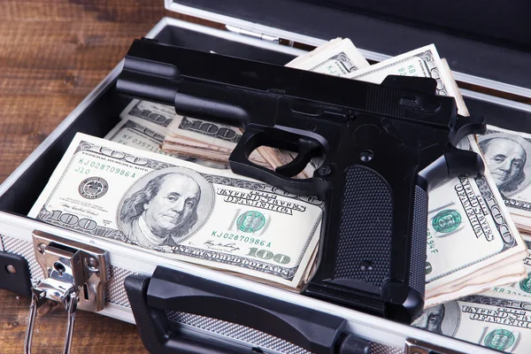 Case with money and gun, on wooden background — Stock Photo, Image