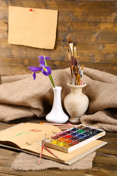 Composition with colorful watercolors, brushes in vase and sketcher on wooden background — Stock Photo, Image