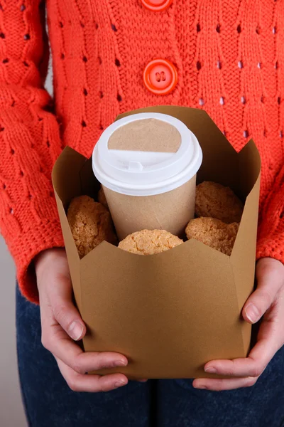 Donna tiene scatola con caffè e biscotti su sfondo grigio — Foto Stock