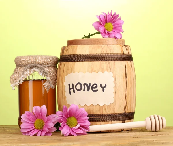 Sweet honey in barrel and jar with drizzler on wooden table on green background — Stock Photo, Image