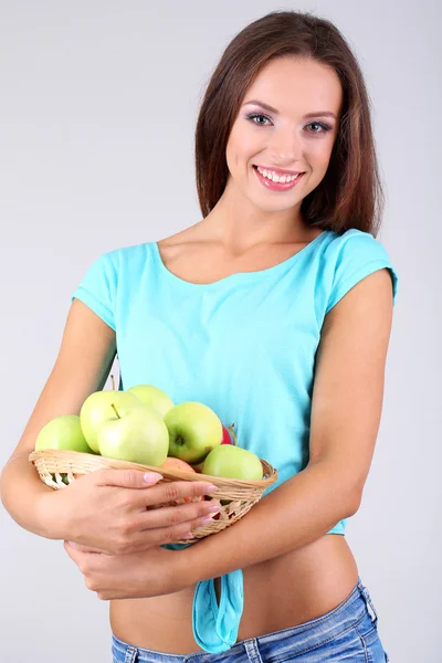 Beautiful young woman with basket of green apples on grey background — Stock Photo, Image