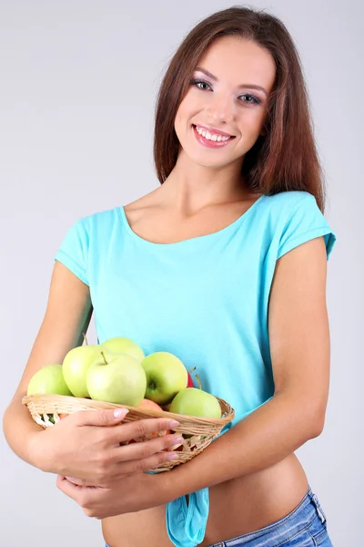 Beautiful young woman with basket of green apples on grey background — Stock Photo, Image