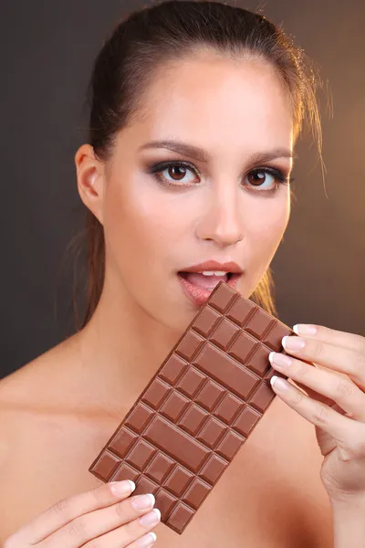 Portret van mooie jonge meisje met chocolade op bruine achtergrond — Stockfoto