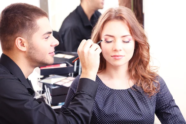 Молодой парень стилист делает макияж красивая женщина в салоне красоты — стоковое фото