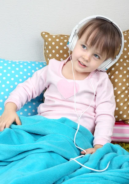 Little girl sitting on pillows on wall background — Stock Photo, Image