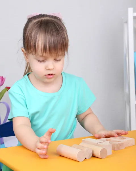 Little girl plays with construction blocks sitting at table in room — Stock Photo, Image