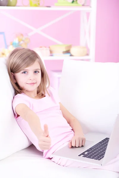 Liten flicka sitter med laptop på soffan i rummet — Stockfoto