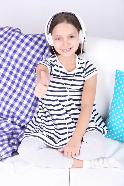 Beautiful little girl sitting on sofa  and listening to music, on home interior background — Stock Photo, Image