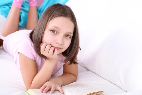 Hermosa niña sentada en el sofá con libro, en el fondo interior de casa — Foto de Stock