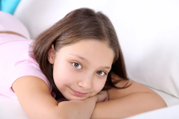 Hermosa niña sentada en el sofá con libro, en el fondo interior de casa —  Fotos de Stock