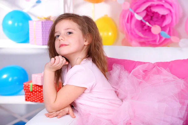 Pretty little girl sitting on sofa on celebratory background — Stock Photo, Image