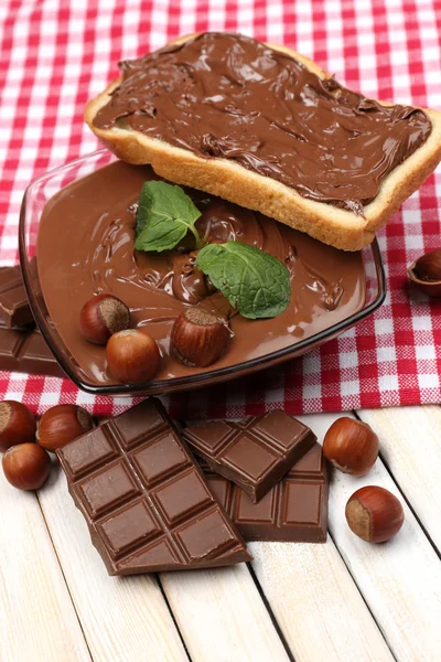 Γλυκιά σοκολάτα φουντούκι εξαπλωθεί με ολόκληρους καρπούς με κέλυφος και μέντα σε ξύλινα φόντο — Φωτογραφία Αρχείου