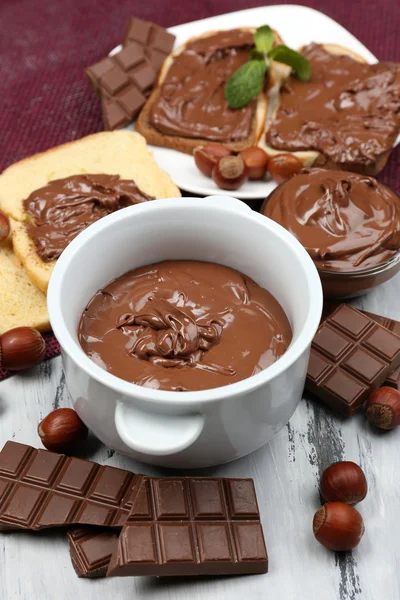 Avelã de chocolate doce espalhada com nozes inteiras e hortelã em fundo de madeira — Fotografia de Stock