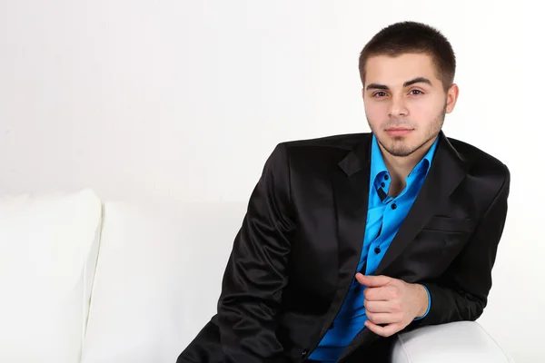 Handsome young man sitting on sofa on light background — Stock Photo, Image