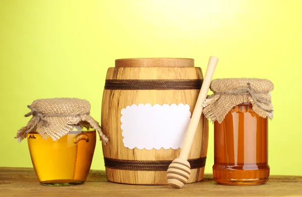 Sweet honey in jars and barrel with drizzler on wooden table on green background — Stok fotoğraf