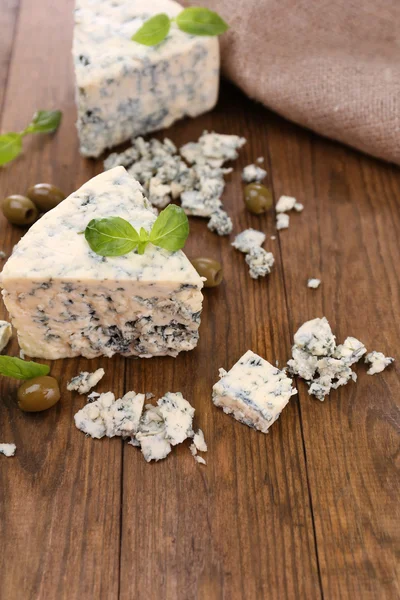 Tasty blue cheese with olives and basil, on wooden table — Stock Photo, Image