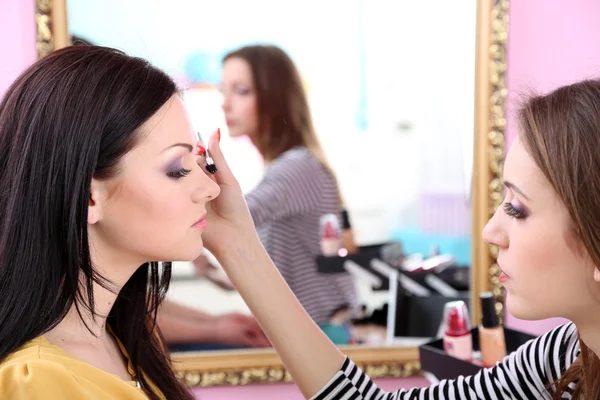 Mladá žena kadeřnice dělá make-up krásnou dívku v salonu krásy — Stock fotografie