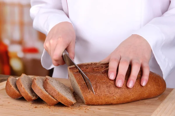 Cutting bread on wooden board on bright background — Stock Photo, Image