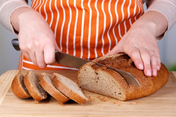 Cutting bread on wooden board on bright background — Stock Photo, Image