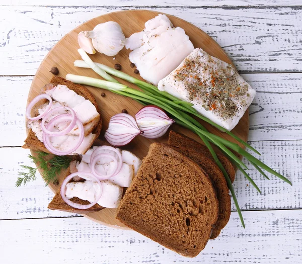 Slices of bread and lard with onion on cutting board on wooden background — Stock Photo, Image