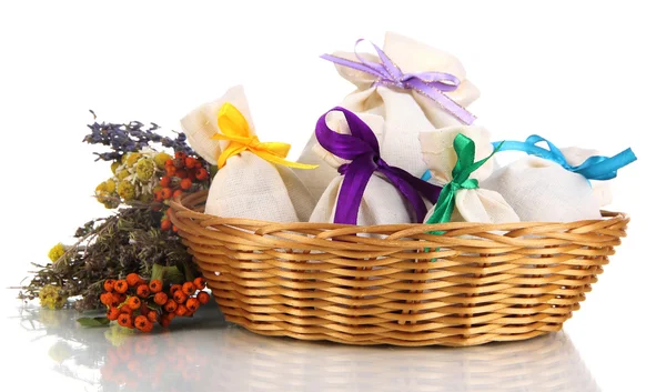 Текстильные пакетики с сушеными цветами, травами и ягодами в плетеной корзине, изолированные на белом — стоковое фото