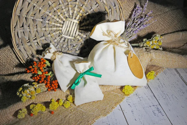 Sachet textile avec fleurs séchées, herbes et baies sur table en bois, sur fond de sac — Photo