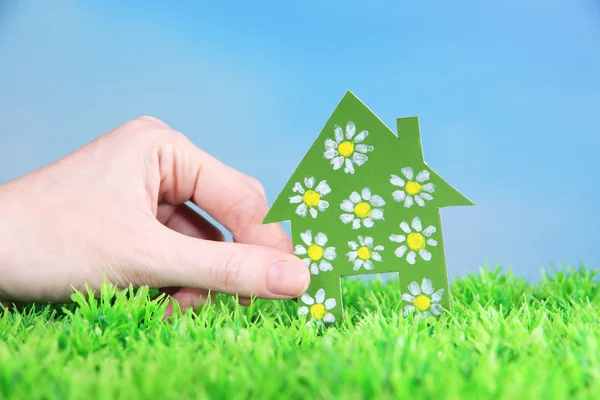 Papier huisje in hand op groen gras op blauwe hemelachtergrond — Stockfoto