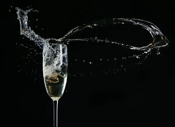 Glass of champagne with splash, on black background — Stock Photo, Image