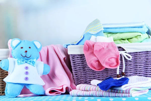 Mucchio di vestiti per bambini nel cestino, sul tavolo sullo sfondo di colore — Foto Stock