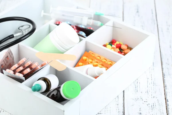 Медицинские таблетки, стетоскоп, ампулы в деревянной коробке, на цветном фоне — стоковое фото