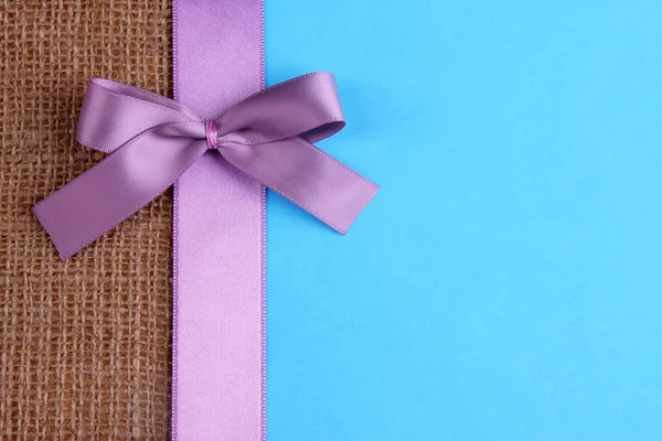 Sackcloth with color ribbon and bow on color paper background — Stock Photo, Image