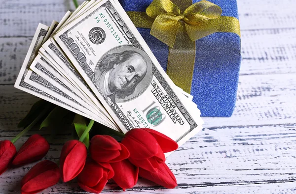 Gift box with money and flowers on color wooden background — Stock Photo, Image