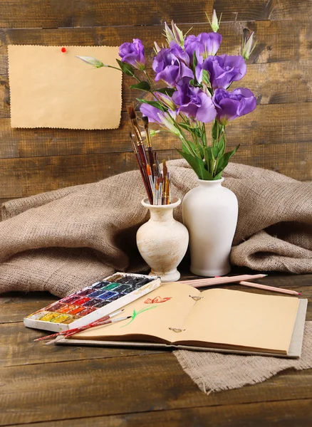 Composizione con acquerelli colorati, pennelli in vaso e schizzo su fondo legno — Foto Stock