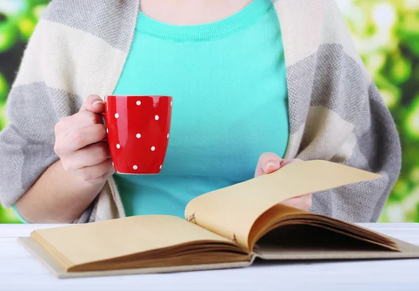 Vrouw leest boek en drinken koffie of thee, close-up — Stockfoto