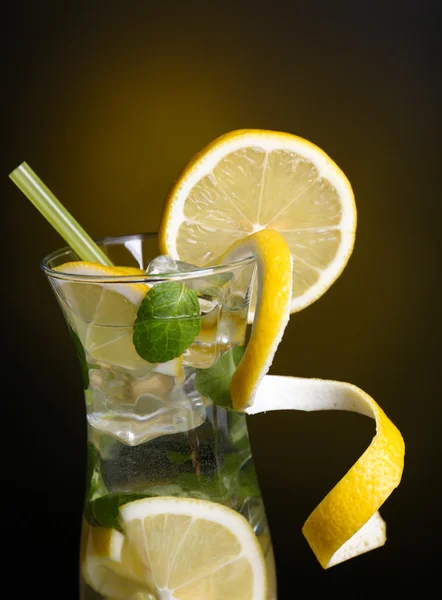 Glass of cocktail with lemon and mint on dark yellow background — Stock Photo, Image