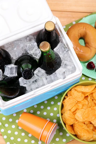 Ice chest full of drinks in bottles on color napkin, on wooden background — Stock Photo, Image