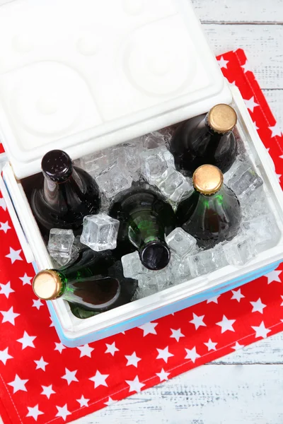 Ice chest full of drinks in bottles on color napkin, on wooden background — Stock Photo, Image