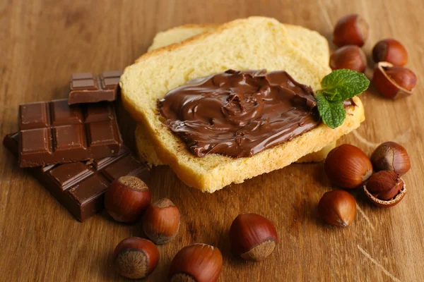 Roti dengan coklat manis hazelnut menyebar di latar belakang kayu — Stok Foto