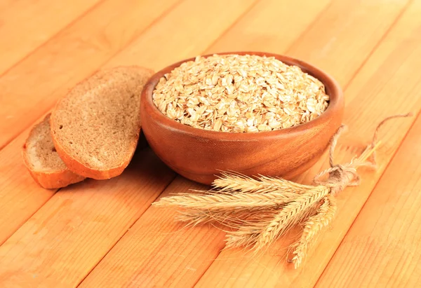 Composition with raw oat-flakes in bowl  and fresh bread slices, on wooden background — Stock Photo, Image