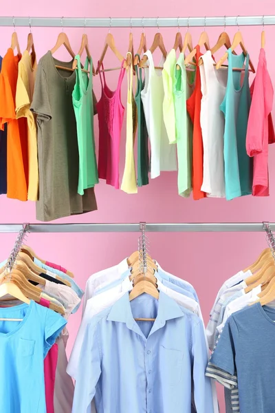 Different clothes on hangers, on pink background — Stock Photo, Image