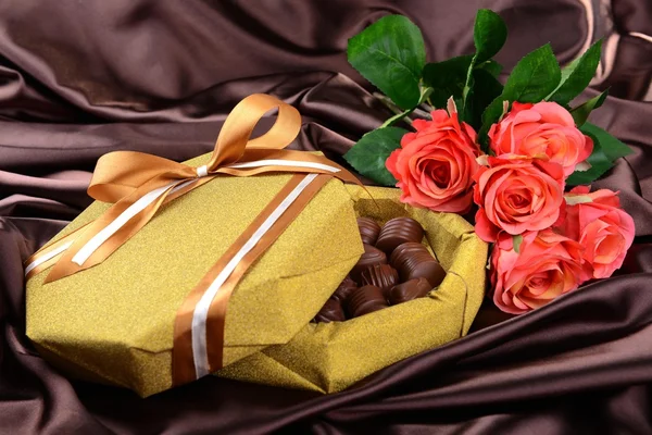 Deliciosos chocolates en caja con flores sobre fondo marrón — Foto de Stock