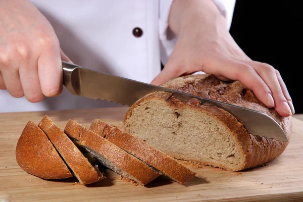 Cutting bread on wooden board on dark background — Stock Photo, Image