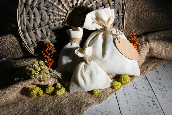 Bolsa de bolsita textil con flores secas, hierbas y bayas sobre mesa de madera, sobre fondo de saco —  Fotos de Stock
