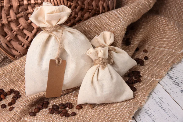 Sacos com grãos de café na mesa de madeira, no fundo de pano de saco — Fotografia de Stock